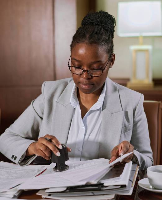 Young businesswoman in eyeglasses and formal suit putting stamp on paper documents after reading and signing new contracts